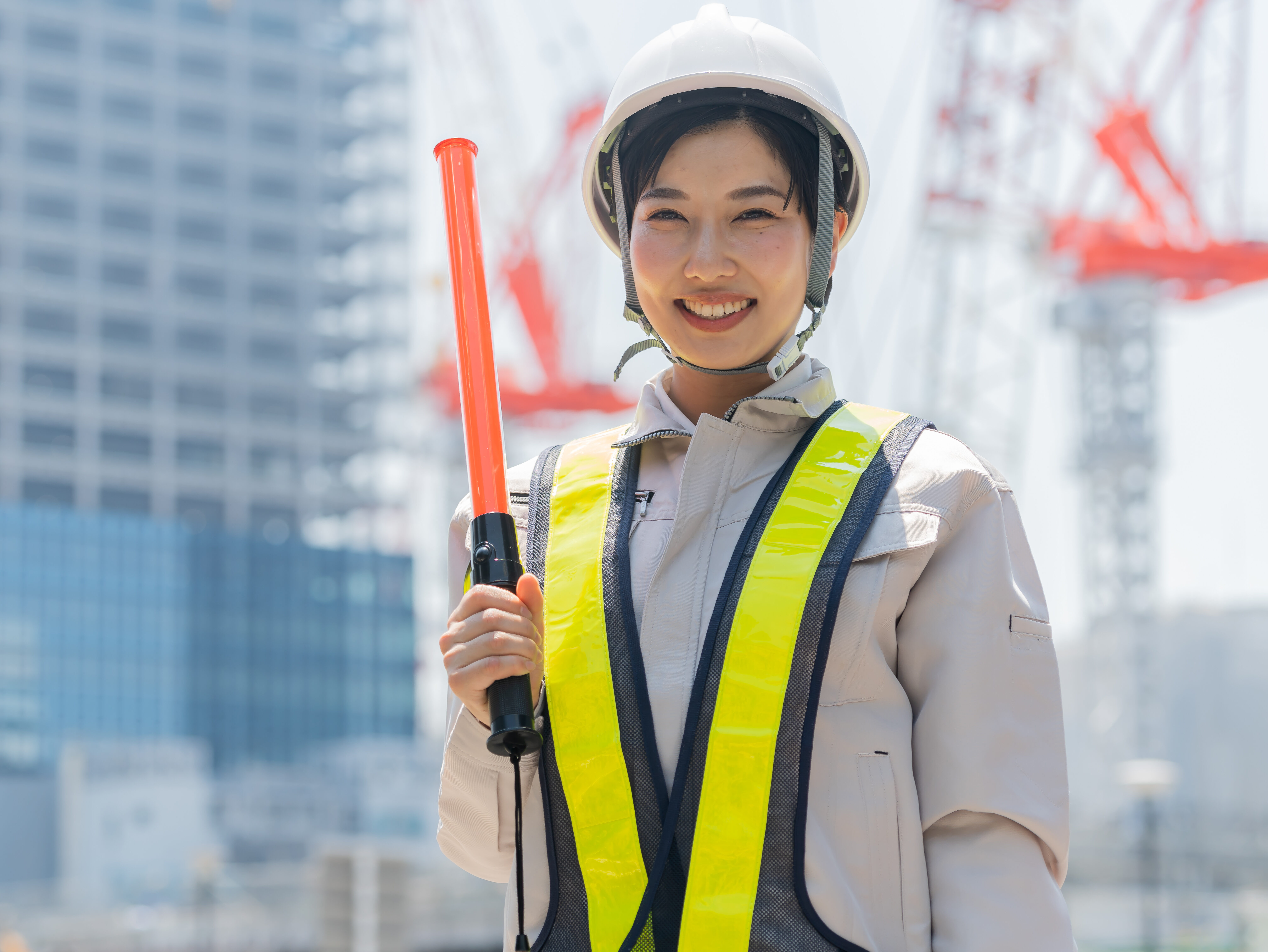 誘導棒を持ち笑顔でカメラを見る工事現場で働く女性